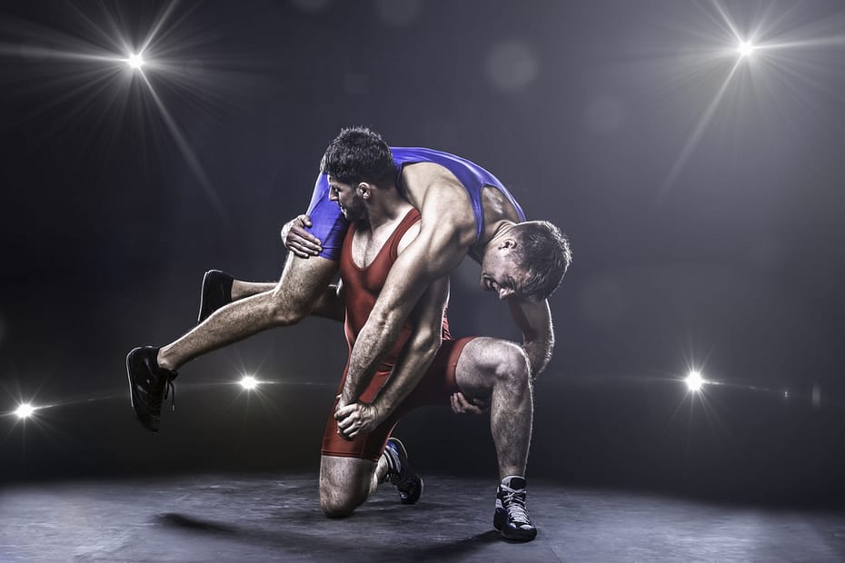 Two freestyle wrestlers in red and blue uniform wrestling against the lights on background. One of them had intacs for keratoconus procedure at Khanna Vision Institute