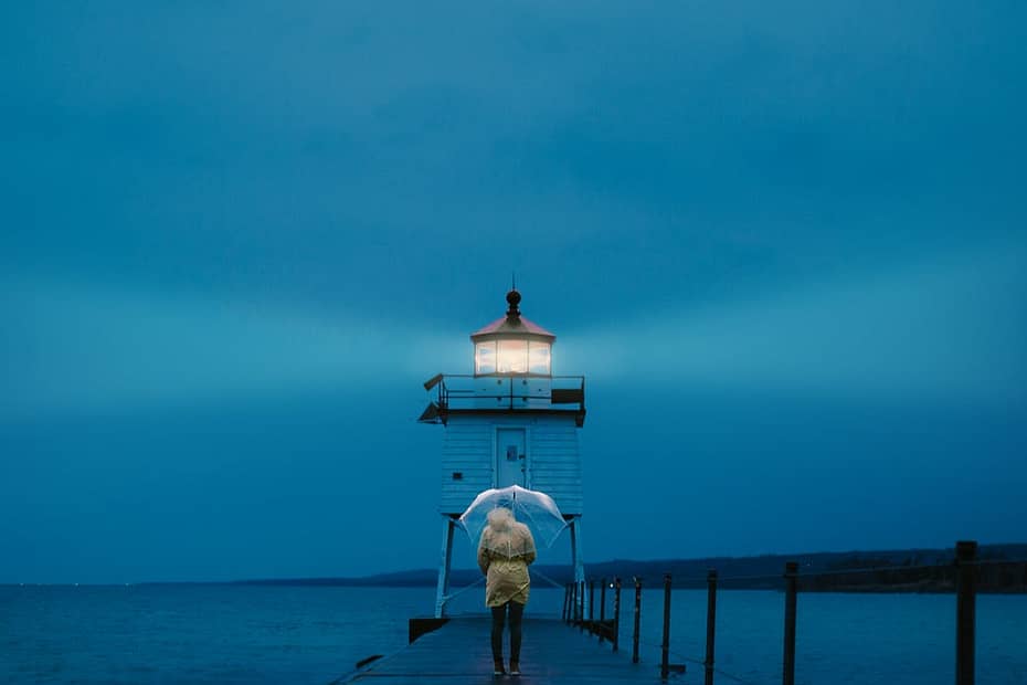 photo of a person standing on footbridge leading to a lighthouse