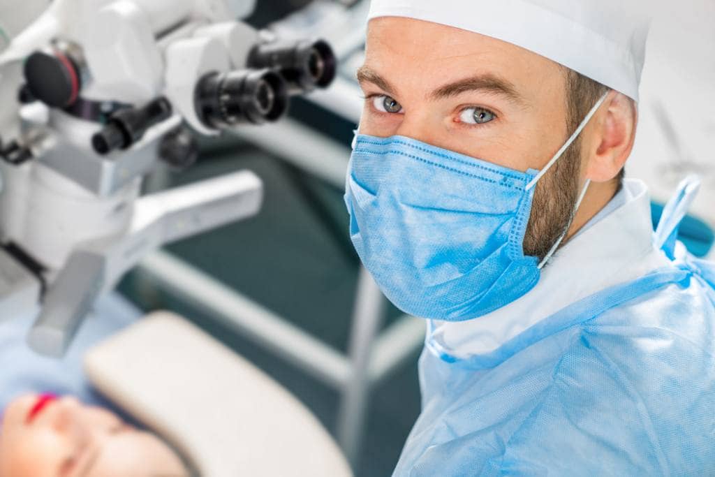 A smiling LASIK surgeon prepares to perform a procedure on his patient
