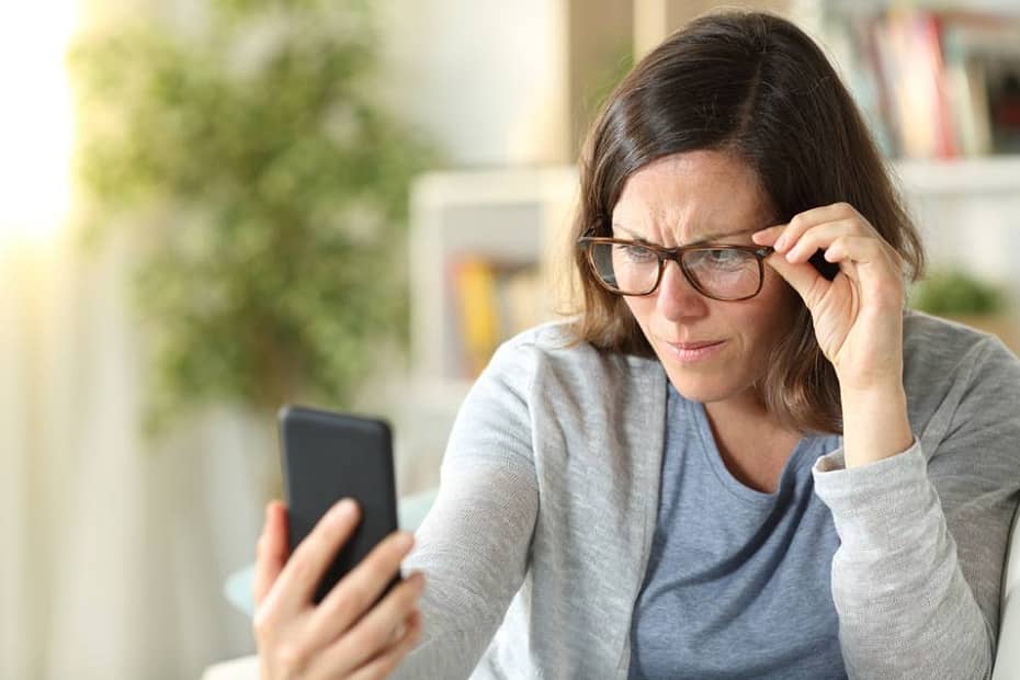 A woman wears reading glasses and struggles to read text on a phone screen